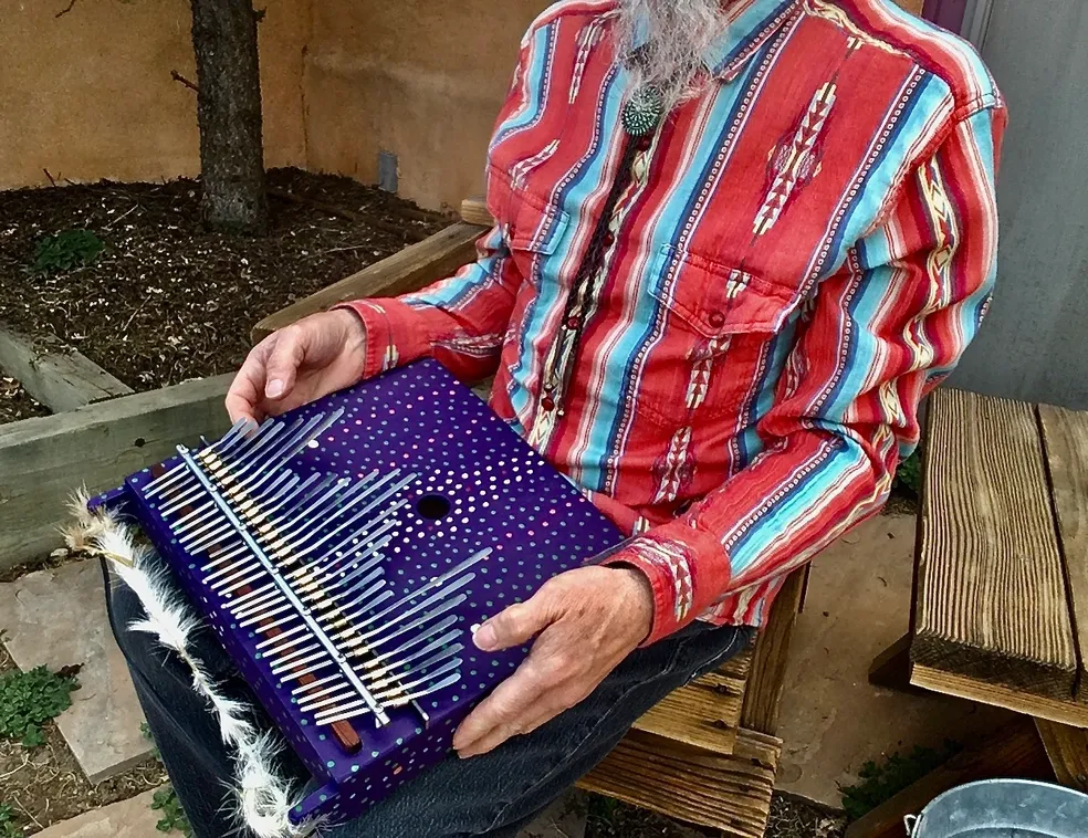 A man sitting on a bench holding a purple accordion and playing Kongoma.