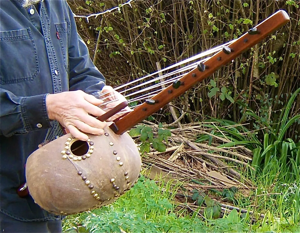 A man holding a Ngoma, a traditional African musical instrument, in the grass.