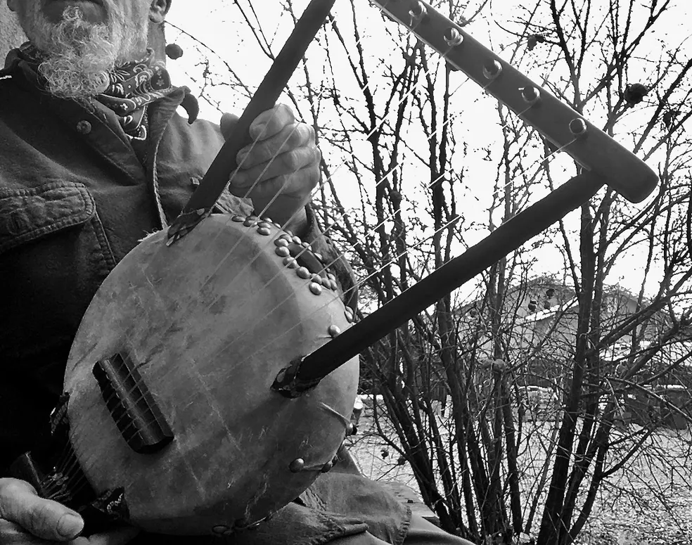 A man sitting on a bench holding a banjo and playing a Kalimba.