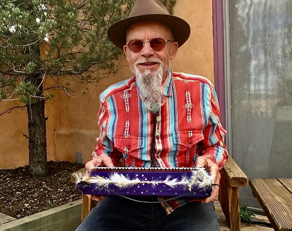 A man in a hat holding a box of feathers, surrounded by the rhythmic sounds of Kongoma drums.