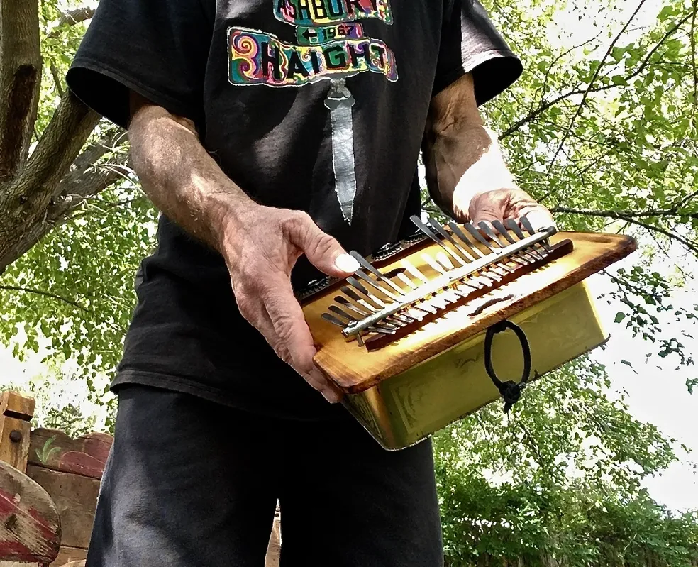 A man in a black shirt holding a wooden box filled with Ngoma, an African music instrument.