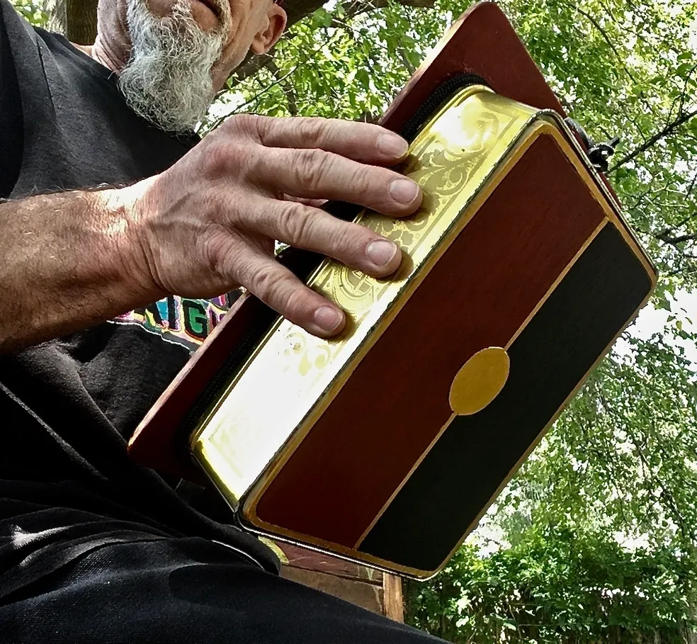 A man sitting on a bench holding a wooden box while listening to Ngoma, African music.