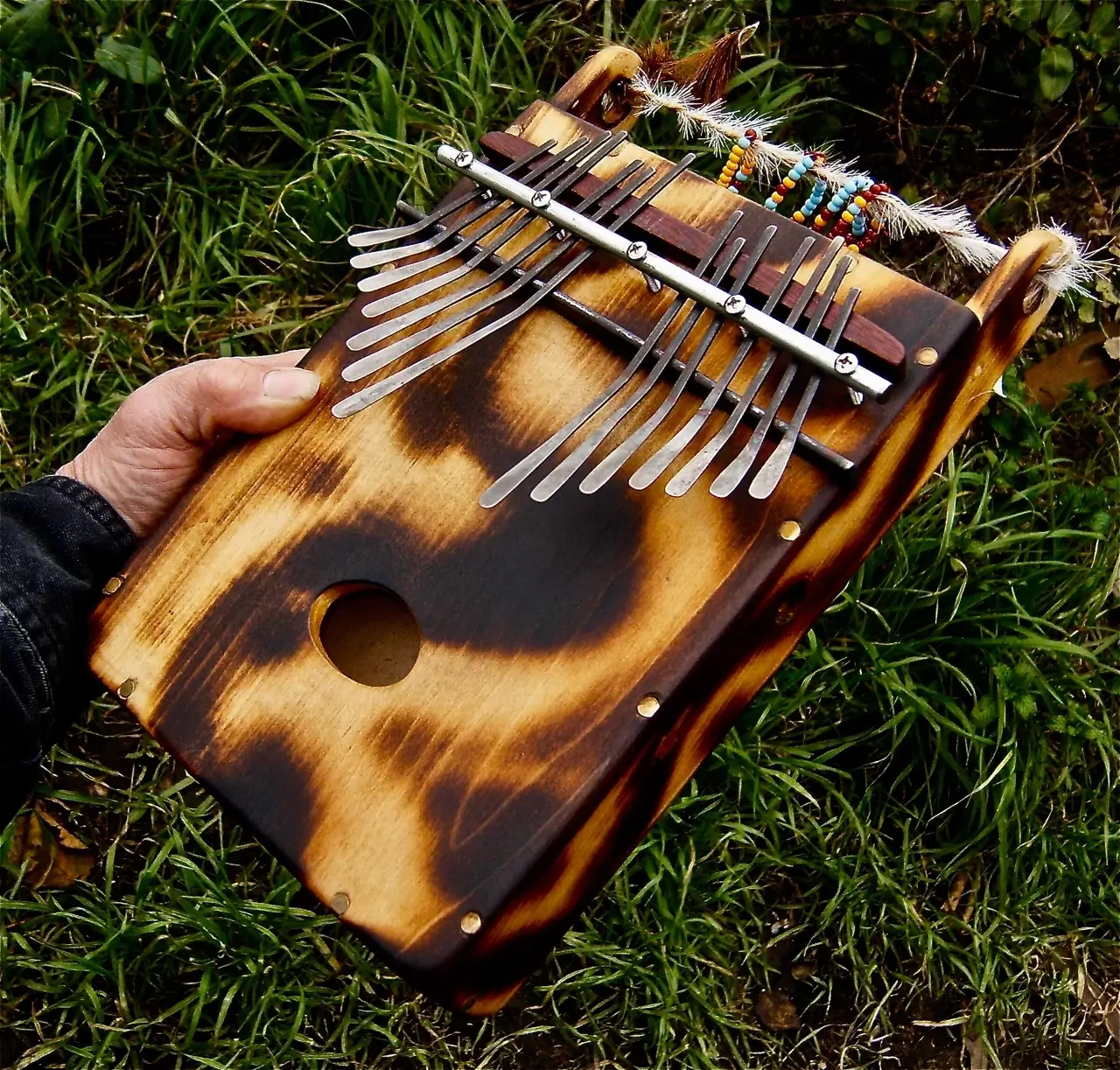 An African person holding a musical instrument in the grass, playing Ngoma - traditional African music.